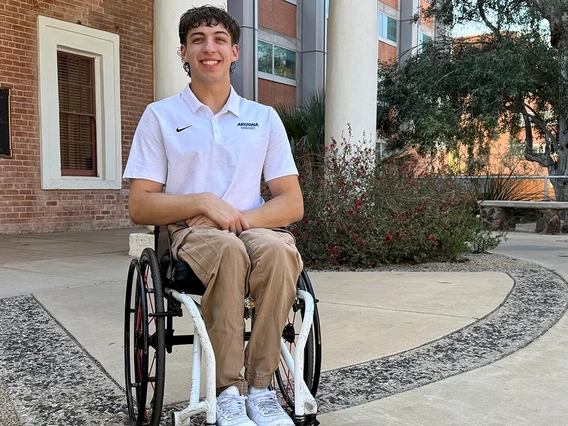 Graduate student Ben Thornton wearing a white Arizona team polo shirt sits smiling in front of building