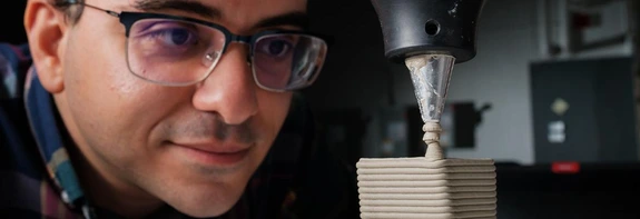 man wearing glasses, looking at 3D printer