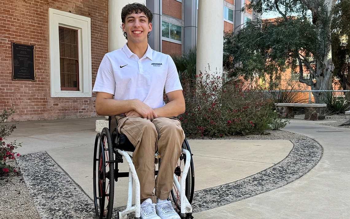 Graduate student Ben Thornton wearing a white Arizona team polo shirt sits smiling in front of building
