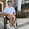 Graduate student Ben Thornton wearing a white Arizona team polo shirt sits smiling in front of building